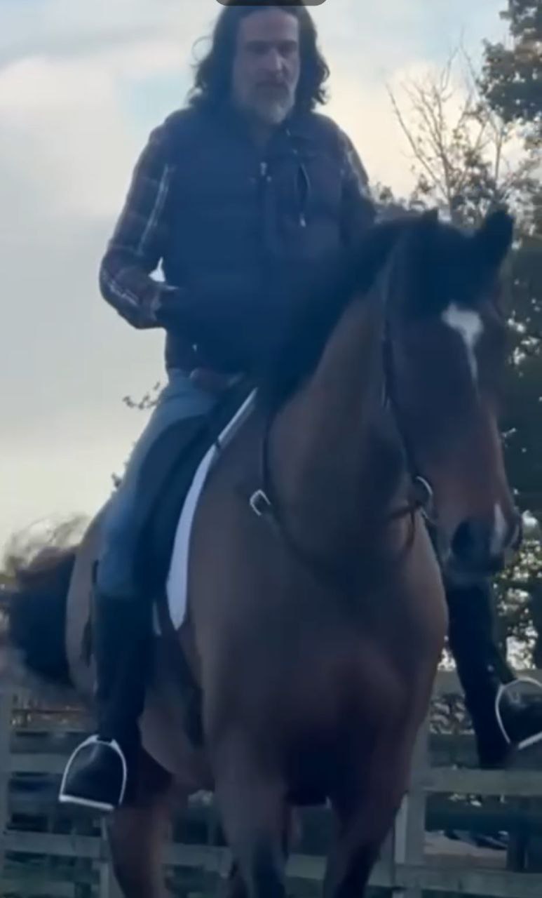 Isaac Ares riding a horse at the walk, demonstrating a classical, balanced seat in a calm outdoor arena.