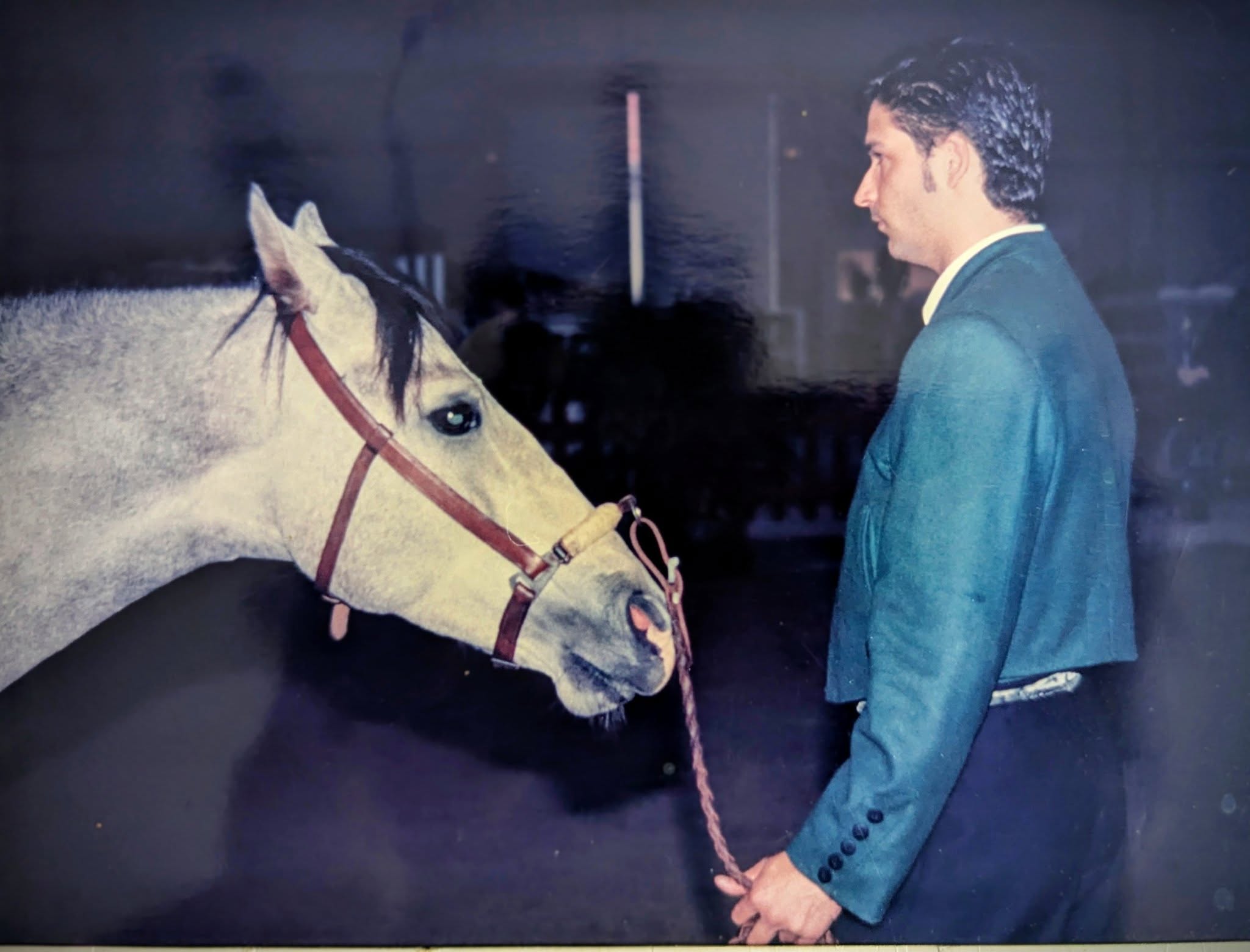 A young Isaac Ares, dressed in a green jacket, shares a calm and focused moment with a grey horse during groundwork, embodying respect and connection.